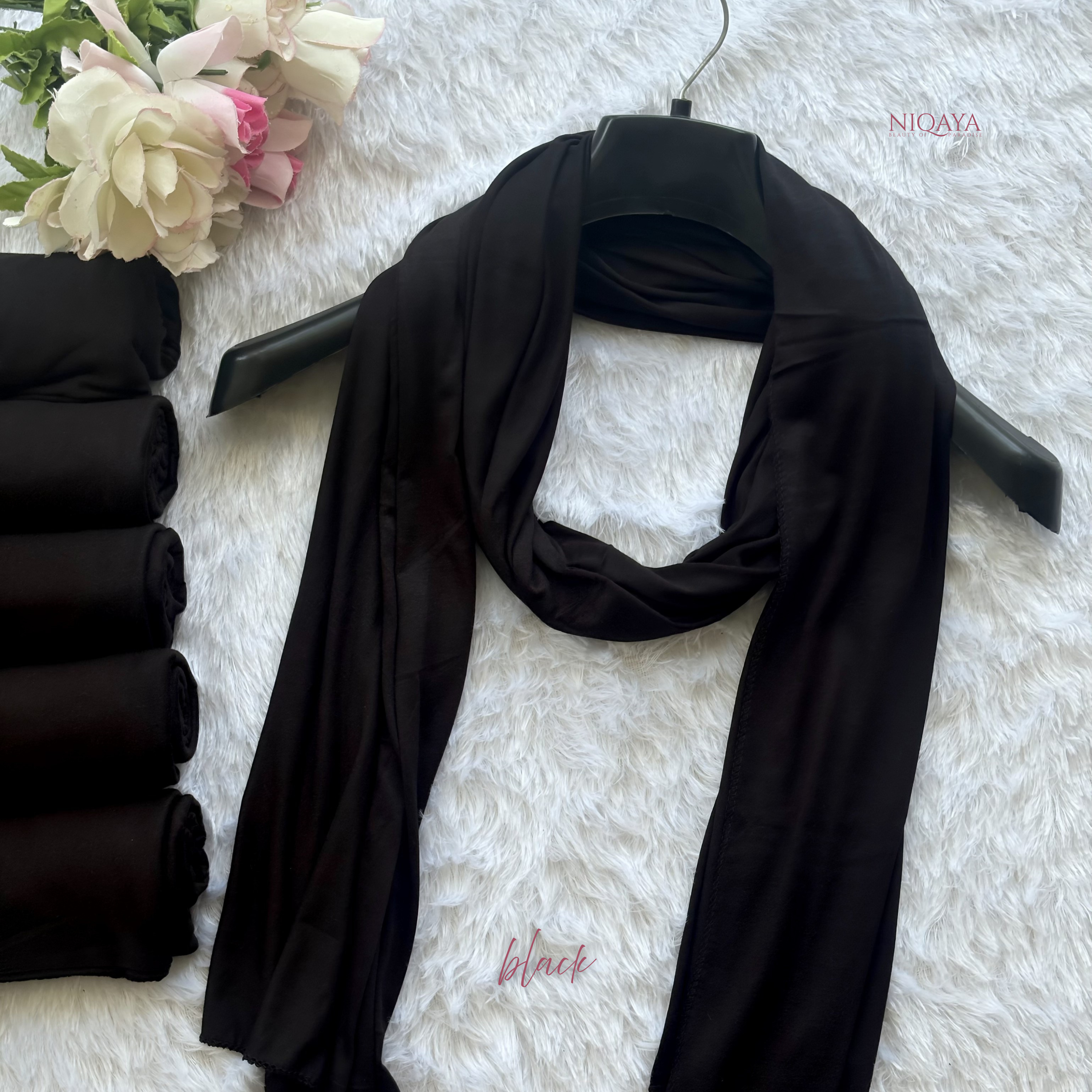 Black scarf on a hanger with flowers and rolled-up scarves on a white background
