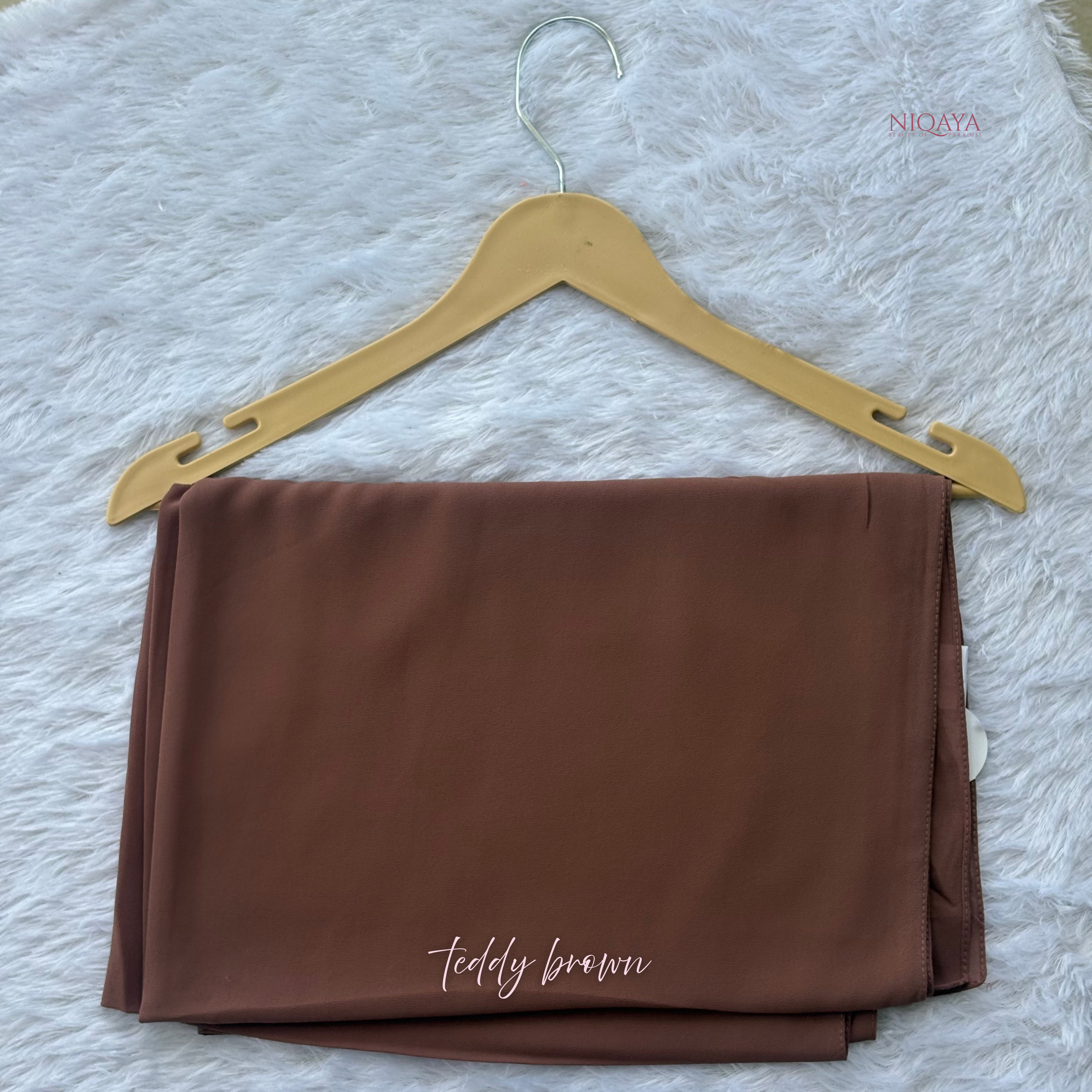 Folded teddy brown fabric on a hanger with 'Niqaya' branding.
