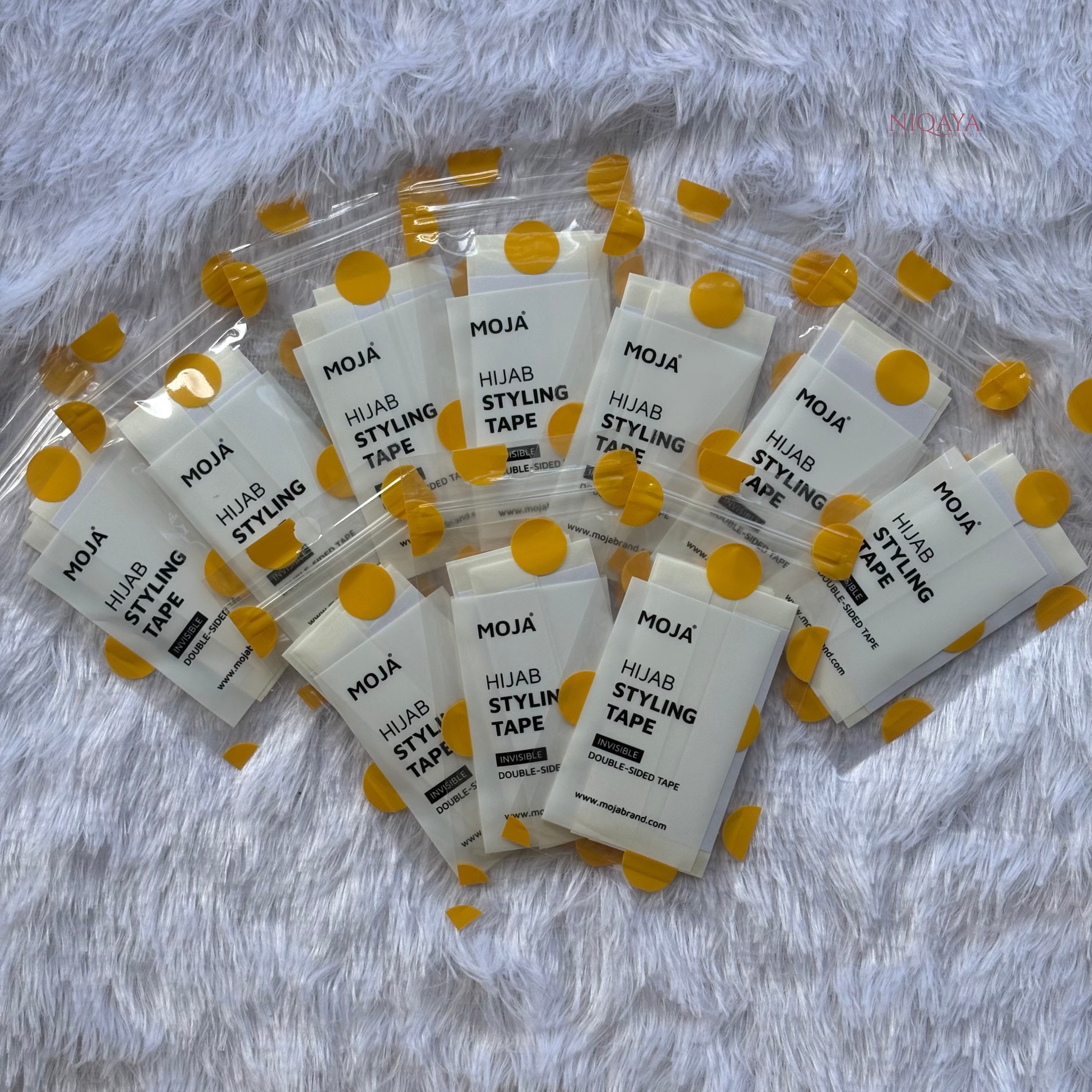 Multiple packages of Moja Hijab Styling Tape on a textured white background