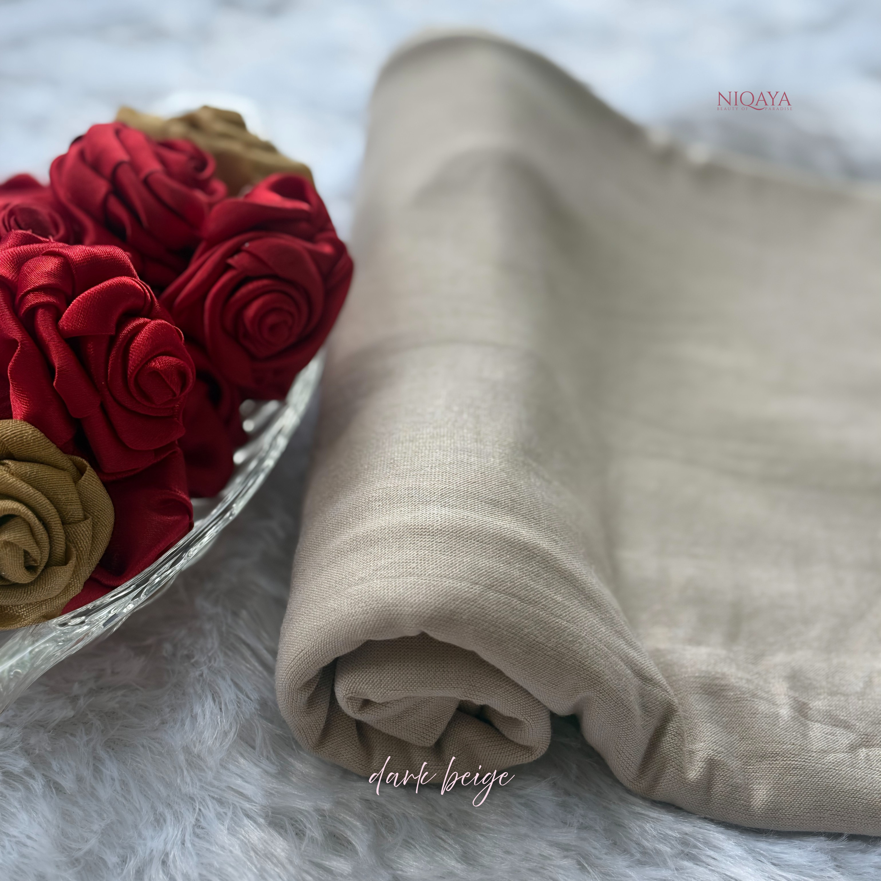 Folded beige fabric next to red and gold flowers on a soft surface