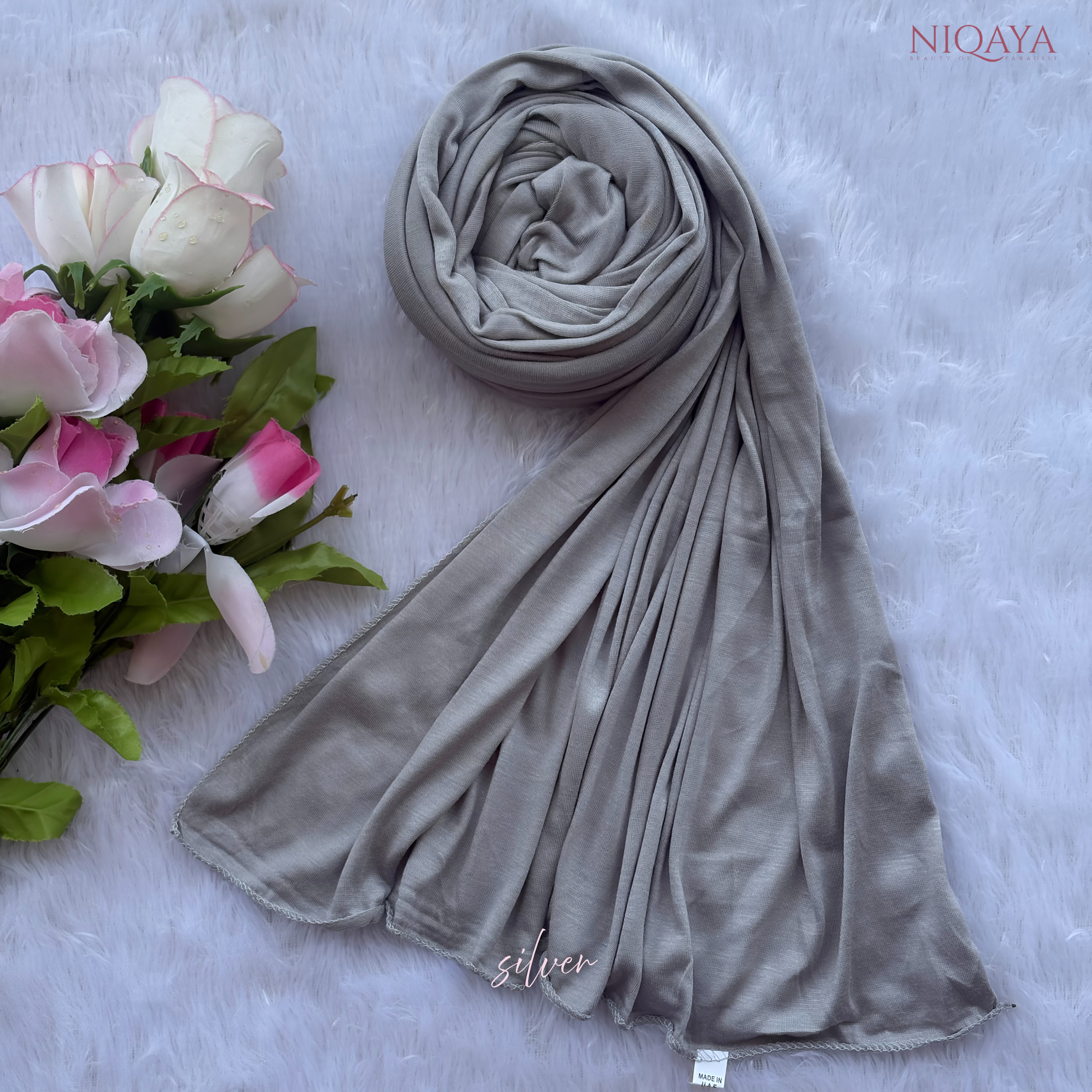 Gray hijab with 'NIQAYA' branding on a light gray background with flowers.