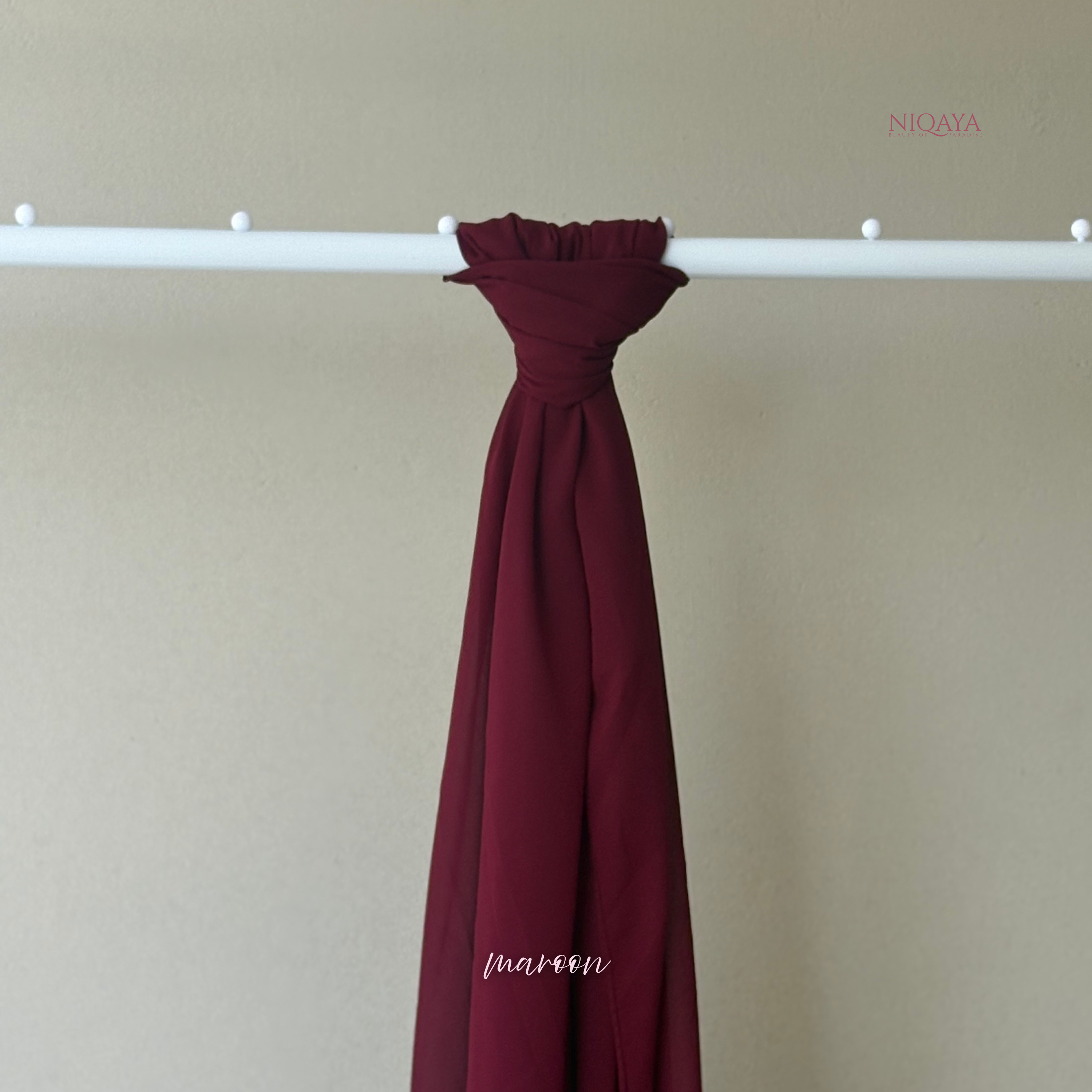 Maroon fabric draped over a white rod against a beige background