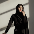 Woman wearing a black hijab and black outfit against a light background
