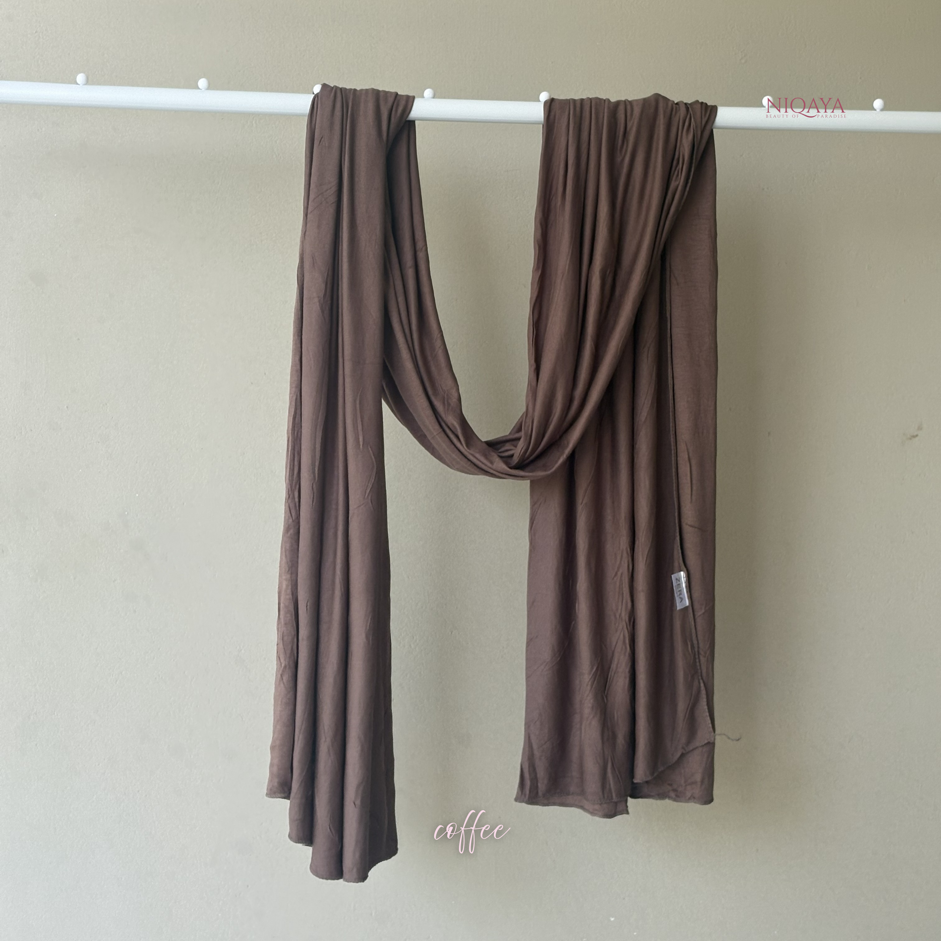 Brown scarf hanging on a white rod against a beige wall