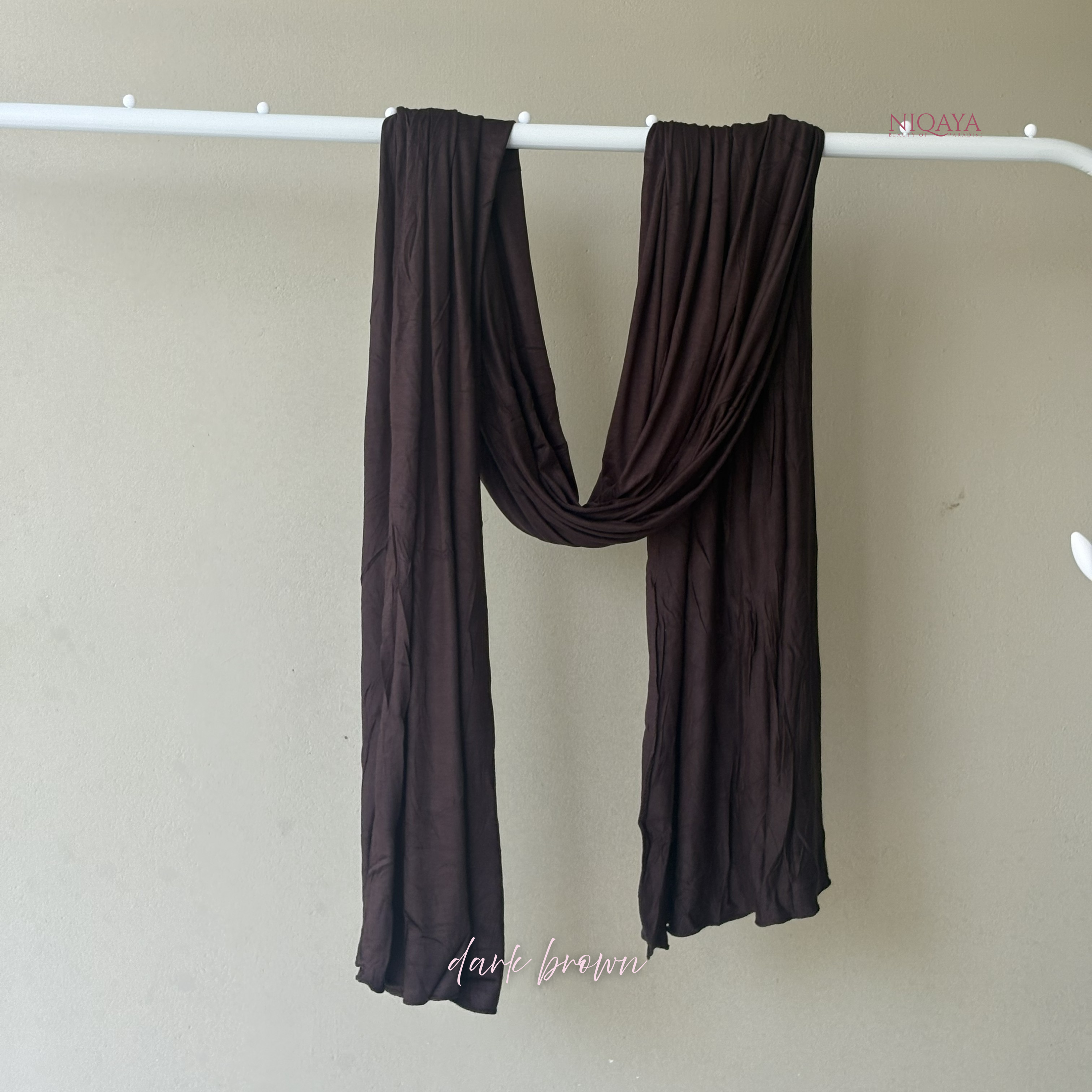Dark brown scarf draped over a white rod against a beige wall.