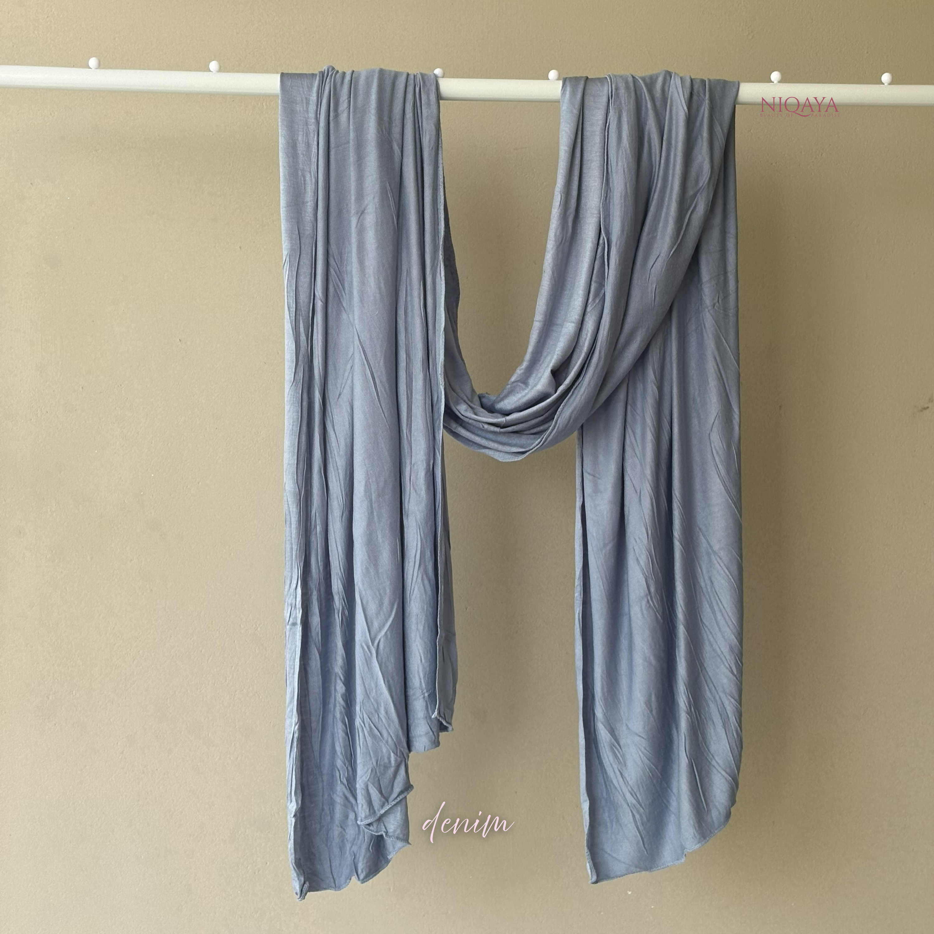 Blue scarf draped over a white rod against a beige background